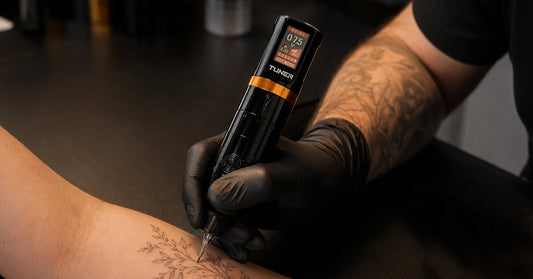 Tattoo artist using Dragoart Tuner tattoo machine for fine line botanical forearm tattoo work.
