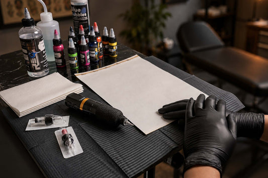 Dragoart Tuner tattoo machine on a professional tattoo workstation with ink bottles, cartridge needles, gloves, and practice skin
