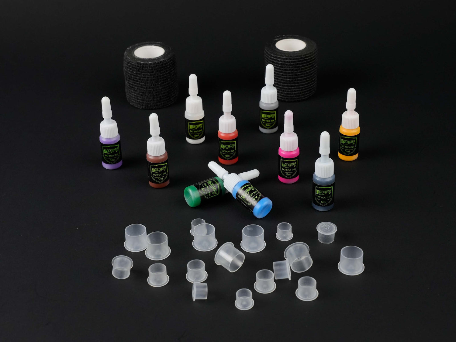 Tattoo kit accessories including colorful 5ml tattoo inks, black cohesive grip tape rolls, and assorted disposable ink caps on black background.