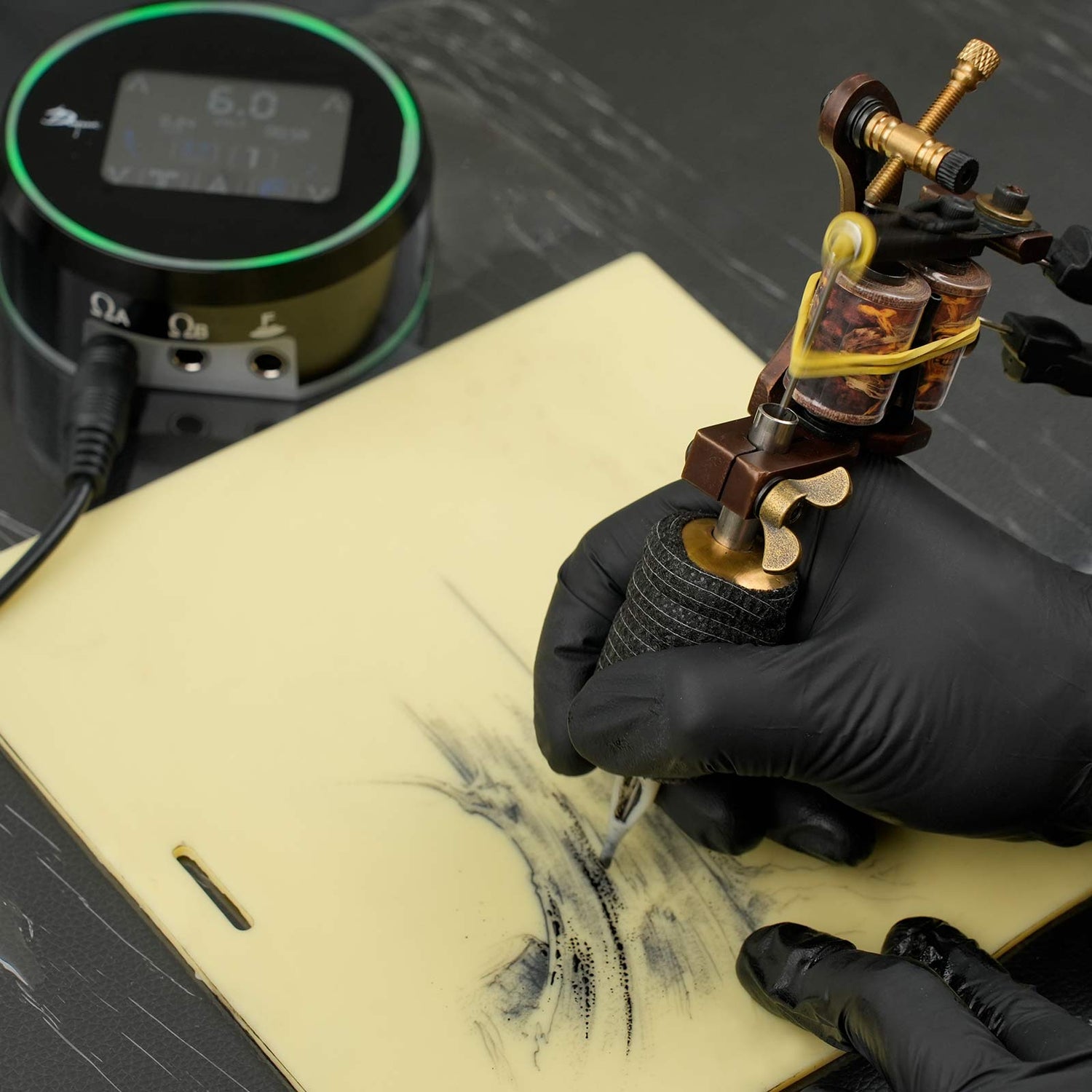 A tattoo artist uses a Dragoart aurora tattoo power supply and a coil machine to do dotwork tattoos on fake skin.