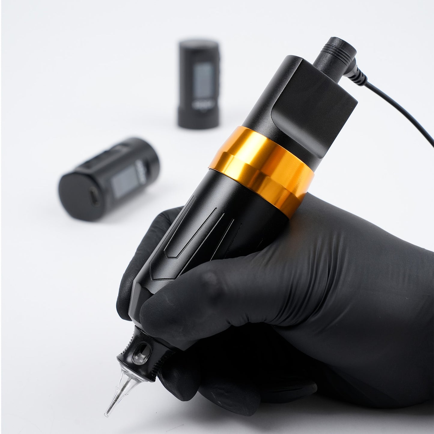 Tattoo artist holding the Dragoart Archer II tattoo pen with RCA cord adapter and two wireless battery packs in the background